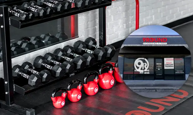 Dumbbells and red kettlebells are neatly arranged on the gym floor, with a window reflecting a 9Round Kickboxing Fitness sign.