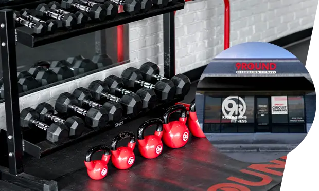 Dumbbells and red kettlebells are neatly arranged on the gym floor, with a window reflecting a 9Round Kickboxing Fitness sign.