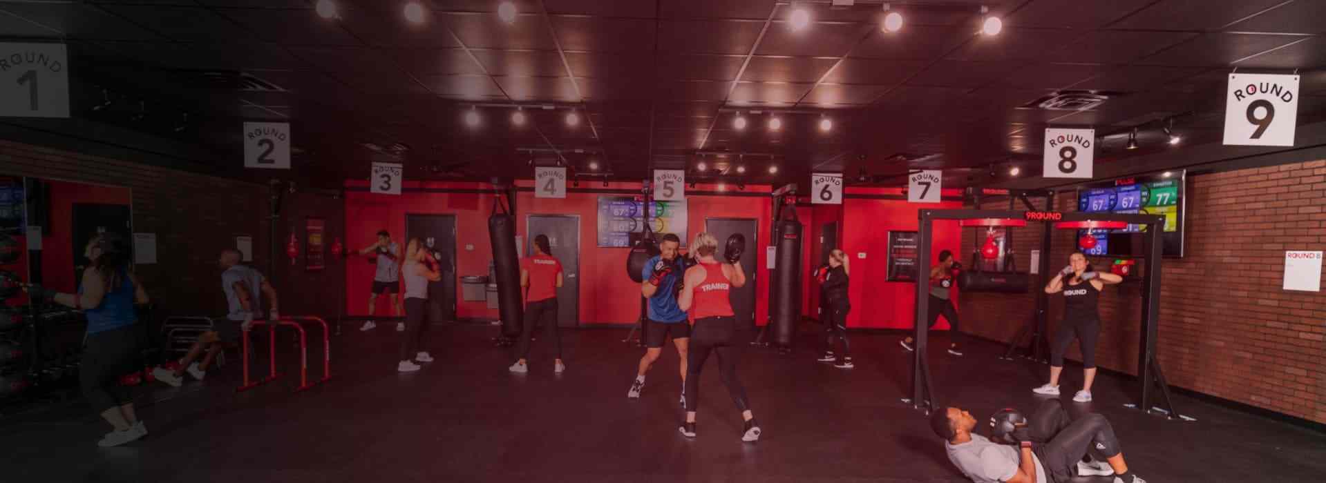 People are working out in a gym, each at different stations labeled 1 to 9. The room is lit with overhead lights and has a dark floor and ceiling.
