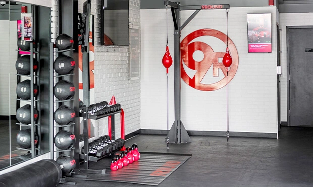 A 9Round gym interior showcasing medicine balls, kettlebells and dumbbells. The floor and walls proudly display the 9Round branding, embodying the energetic spirit of this dynamic fitness franchise.